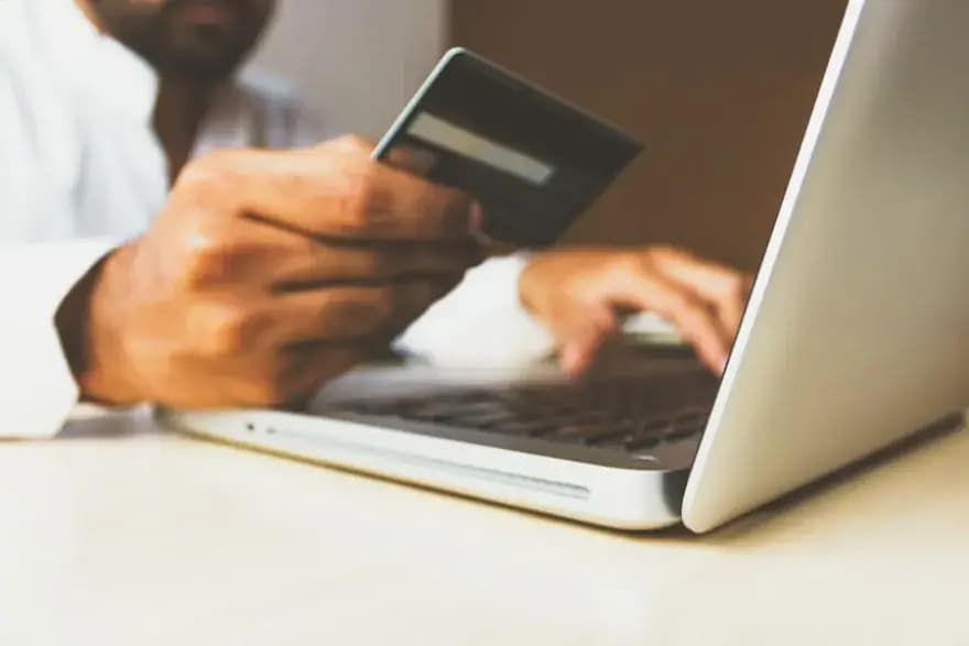 Person bezahlt mit Kreditkarte am Laptop – Online-Shop erstellen lassen